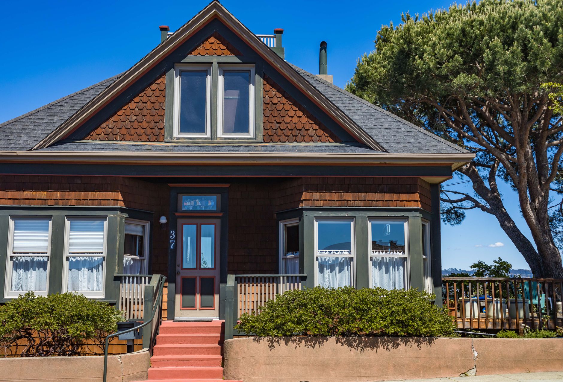 A picturesque vintage house with red stairs, green trims, and bay windows set against a clear blue sky
