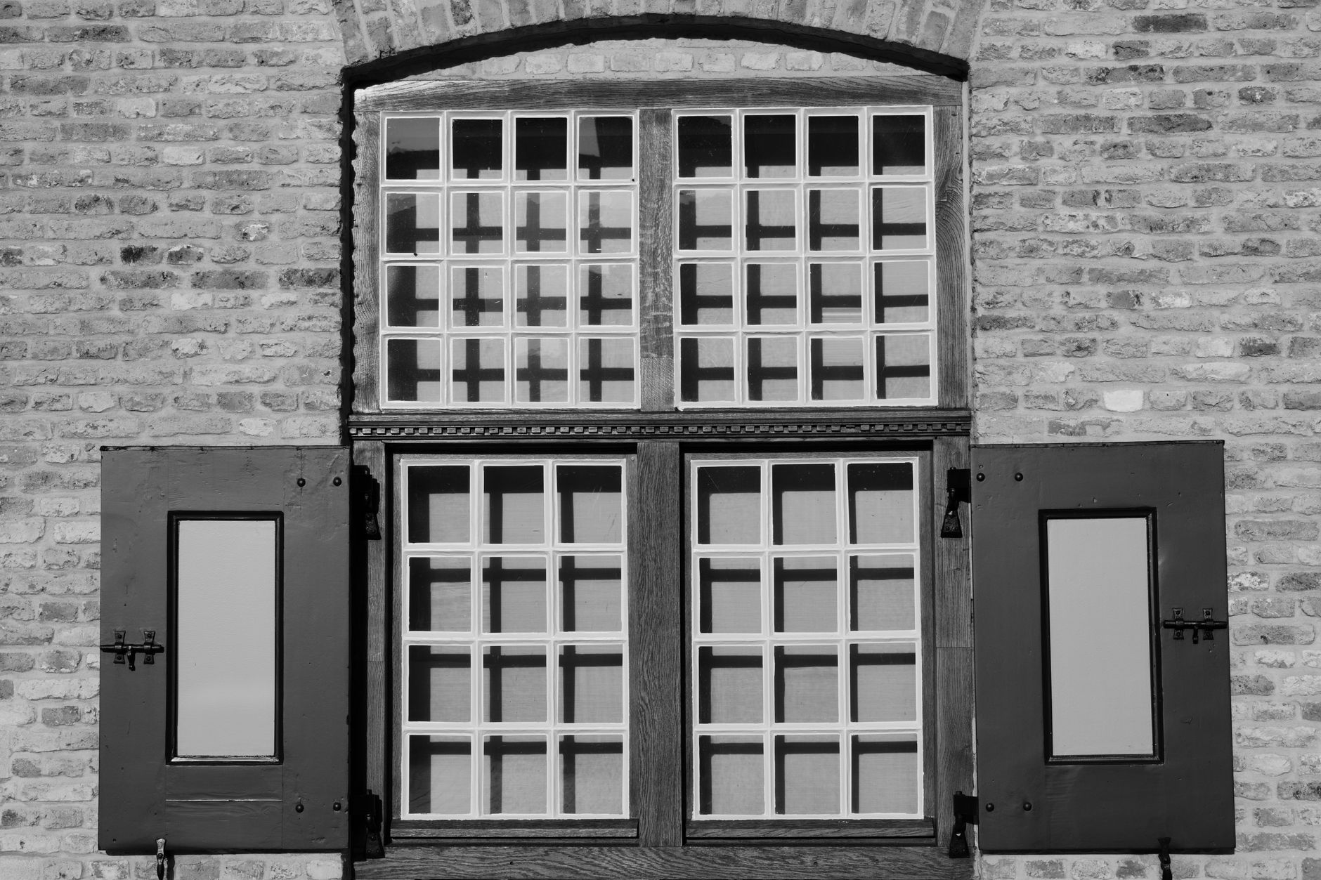 Black and white photo of a classic brick facade featuring wooden shutters and a grid window design