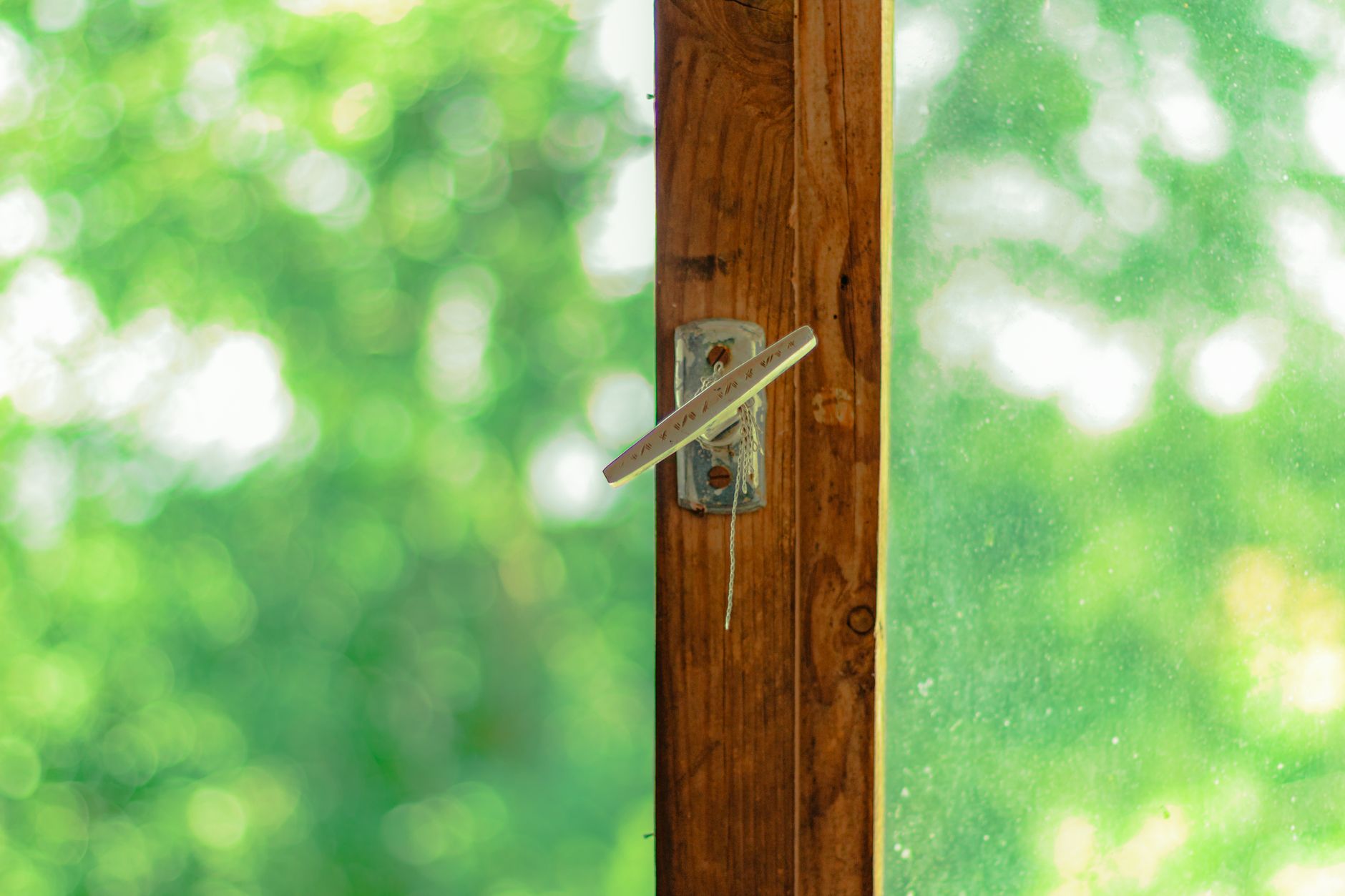 A rustic wooden window showcasing a serene green nature view with soft bokeh in daylight