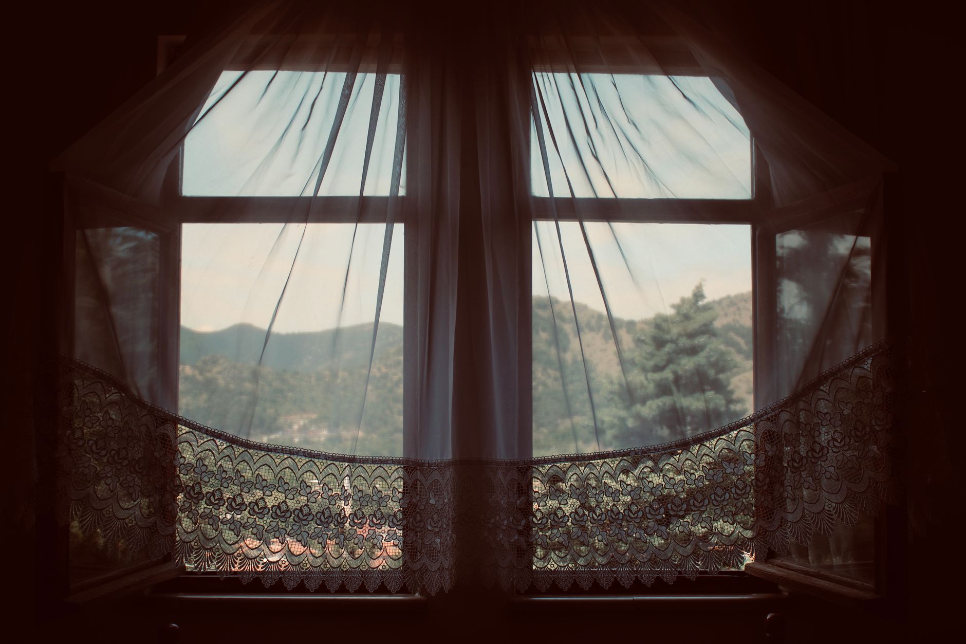 Serene landscape through a vintage window with lace curtains, capturing the peaceful outdoors